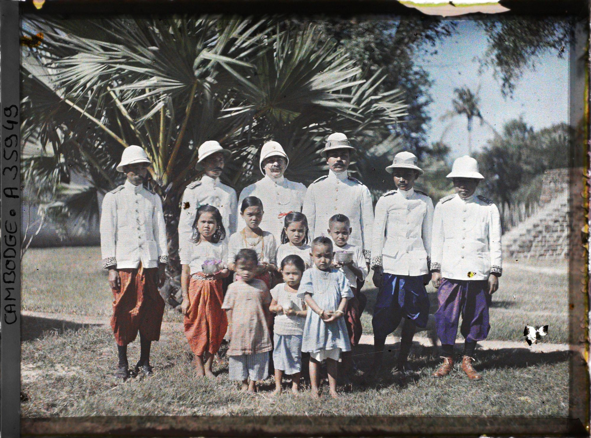 Image représentant Un fonctionnaire du protectorat français entouré de fonctionnaires cambodgiens, accompagnés d'enfants