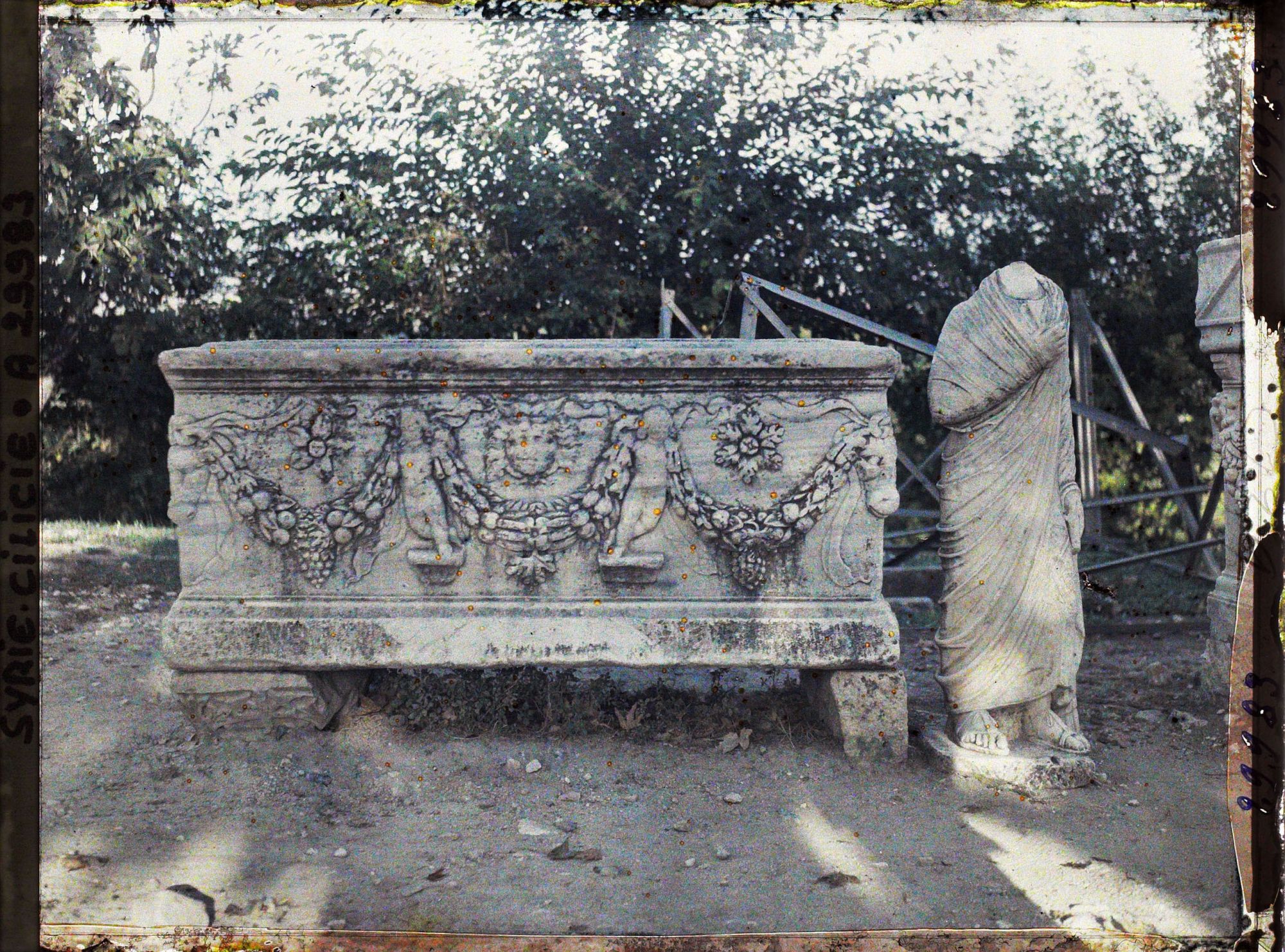 Image représentant Sarcophage romain représentant une décoration végétale, le soleil et Cupidon. A sa droite, une statue acéphale
