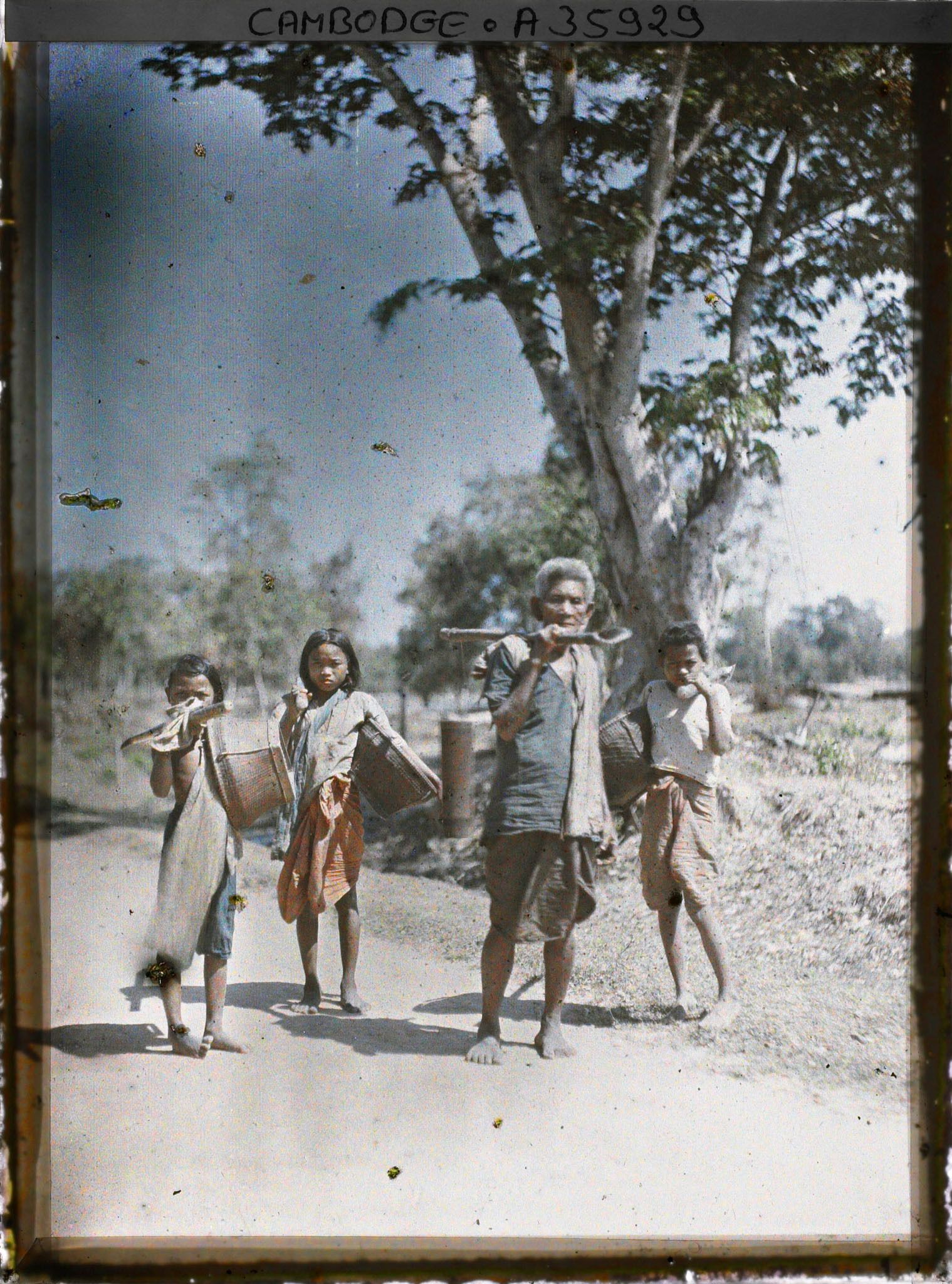 Image représentant Un homme transportant du jus de palme et et des enfants portant des paniers, sur une route