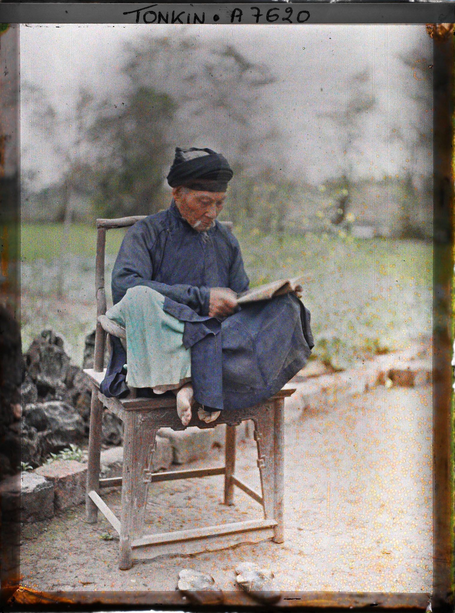 Image représentant Un lettré lisant, assis en tailleur dans un fauteuil en bois
