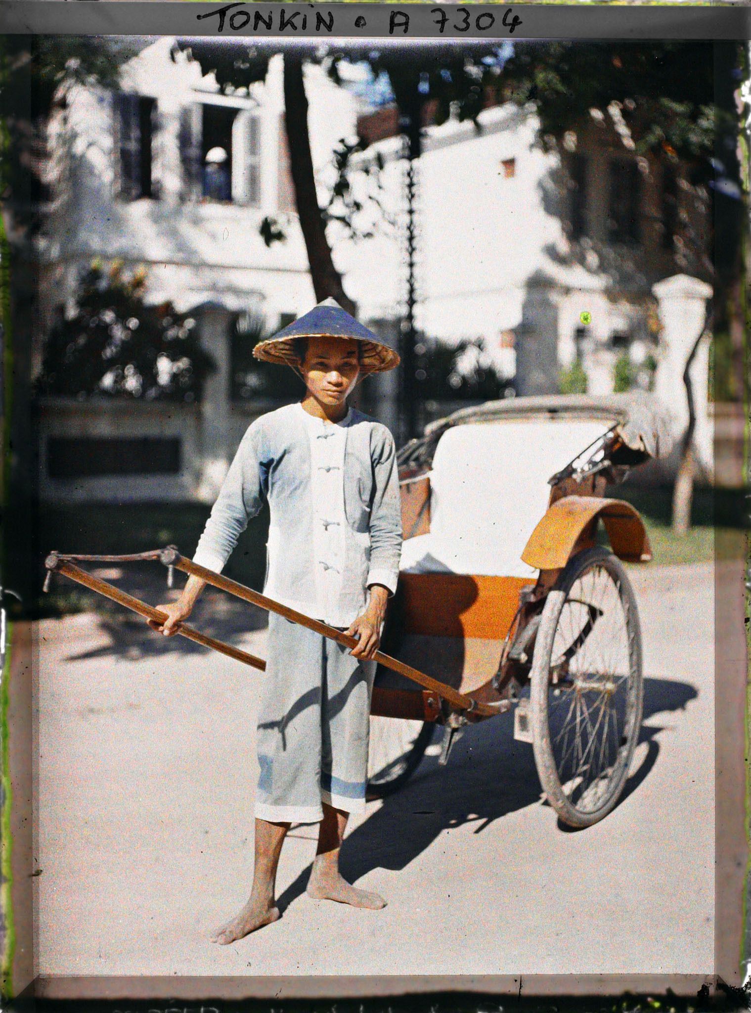 Image représentant Un pousse-pousse à roues caoutchoutées et son tireur, vêtu et coiffé de bleu
