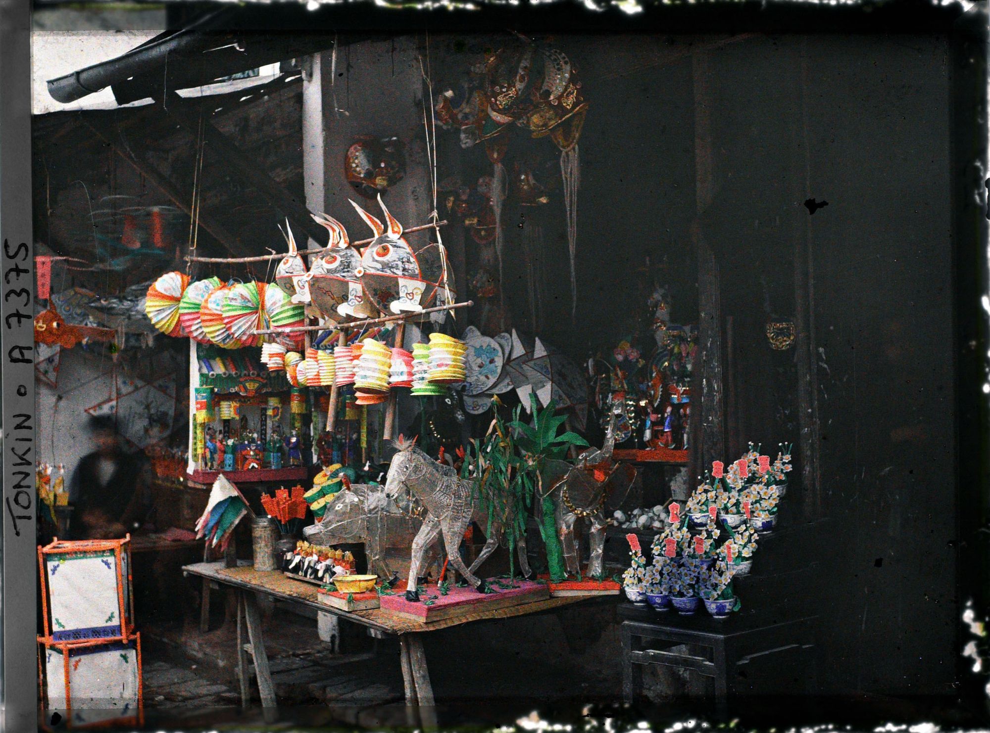 Image représentant Un étalage de jouets en papier huilé devant une boutique, dans la " rue du Chanvre "