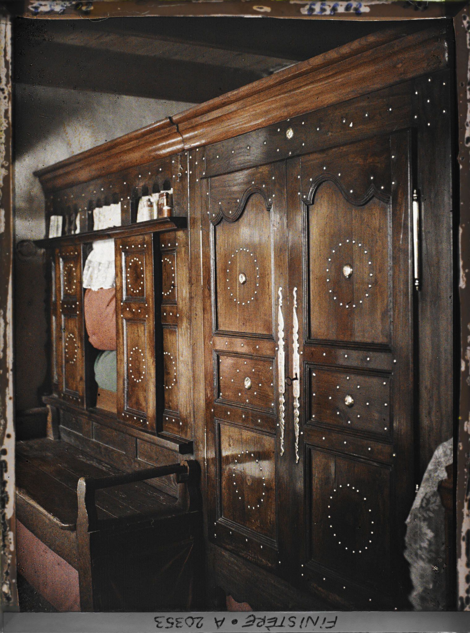 Image représentant Un lit clos à décor clouté avec armoire et banc-coffre