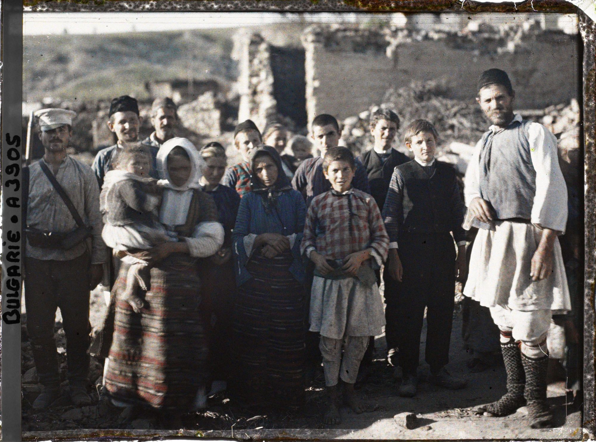 Image représentant Groupe d'hommes, de femmes et d'enfants et un soldat au milieu de décombres du village