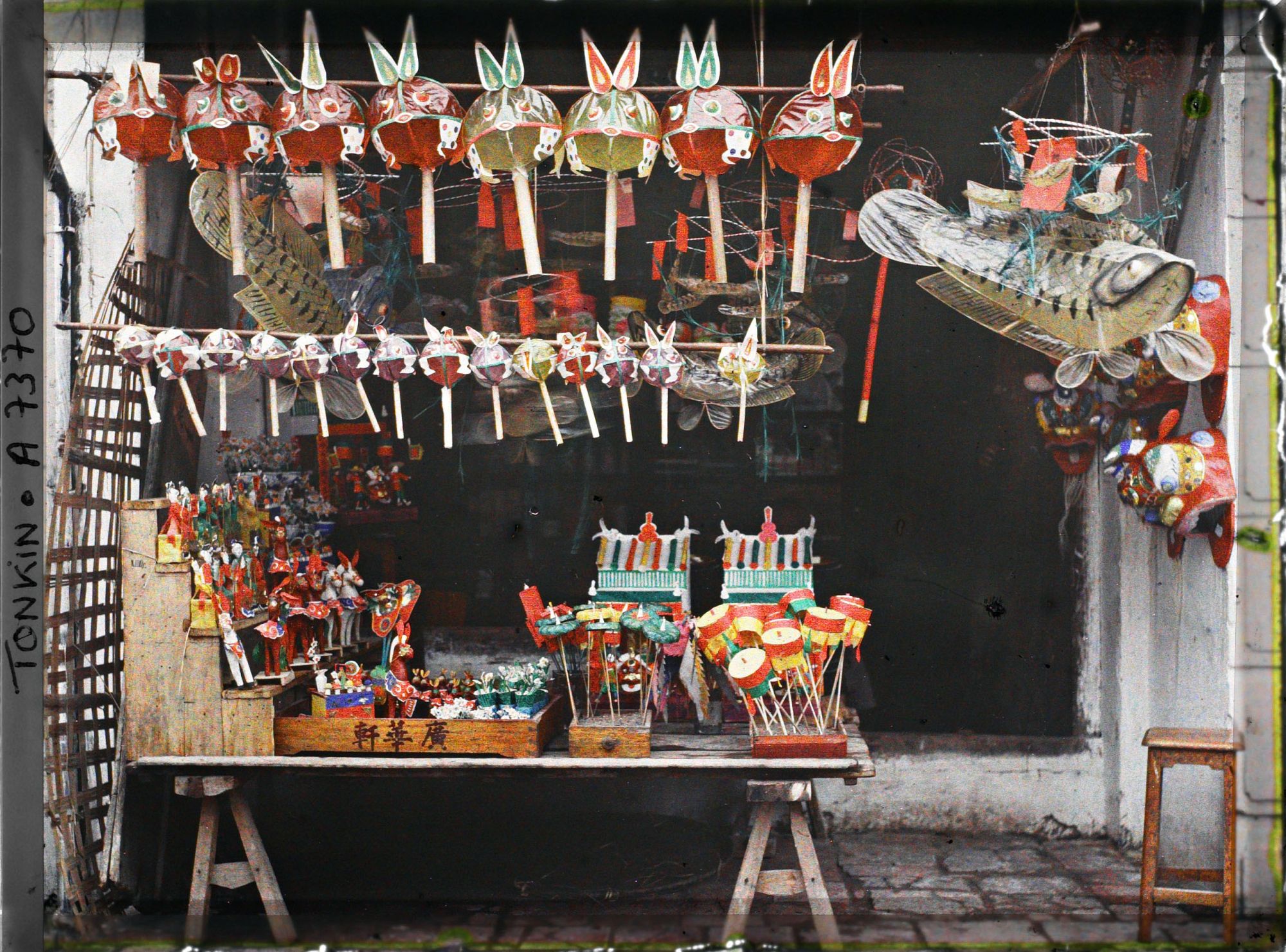 Image représentant Un étalage de jouets en papier huilé devant une boutique, dans la " rue du Chanvre "