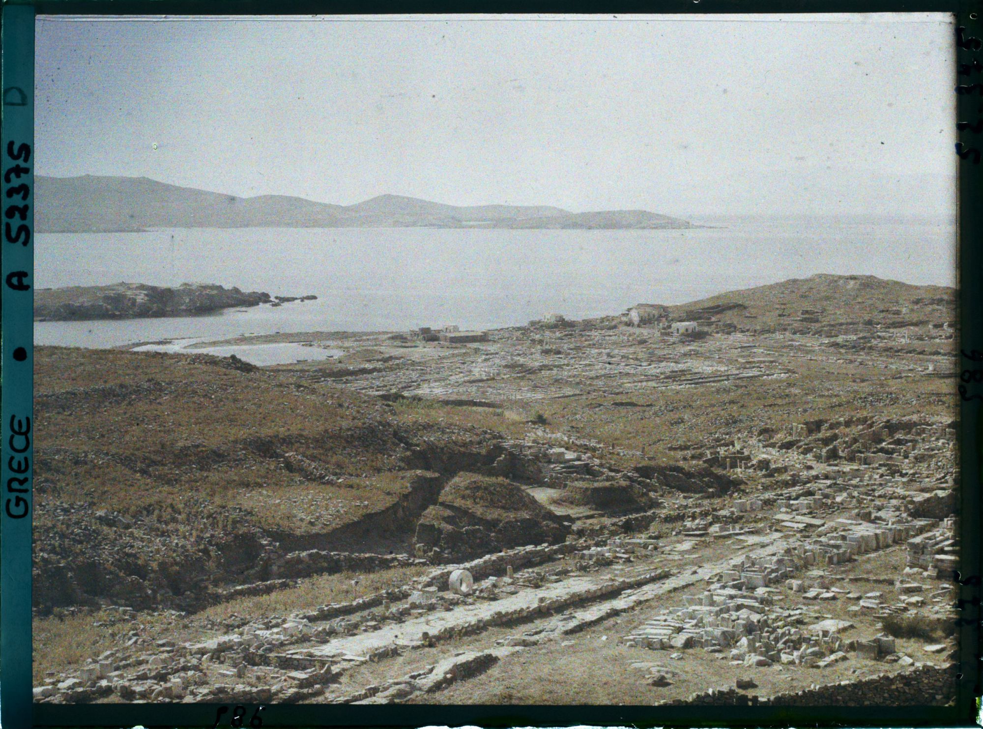 Image représentant Panorama vers les ruines de la ville antique (haute et basse) et la mer depuis l'Antre du Cinthe sur le versant occidental du mont Cinthe (au fond, l'Ile de Syros)