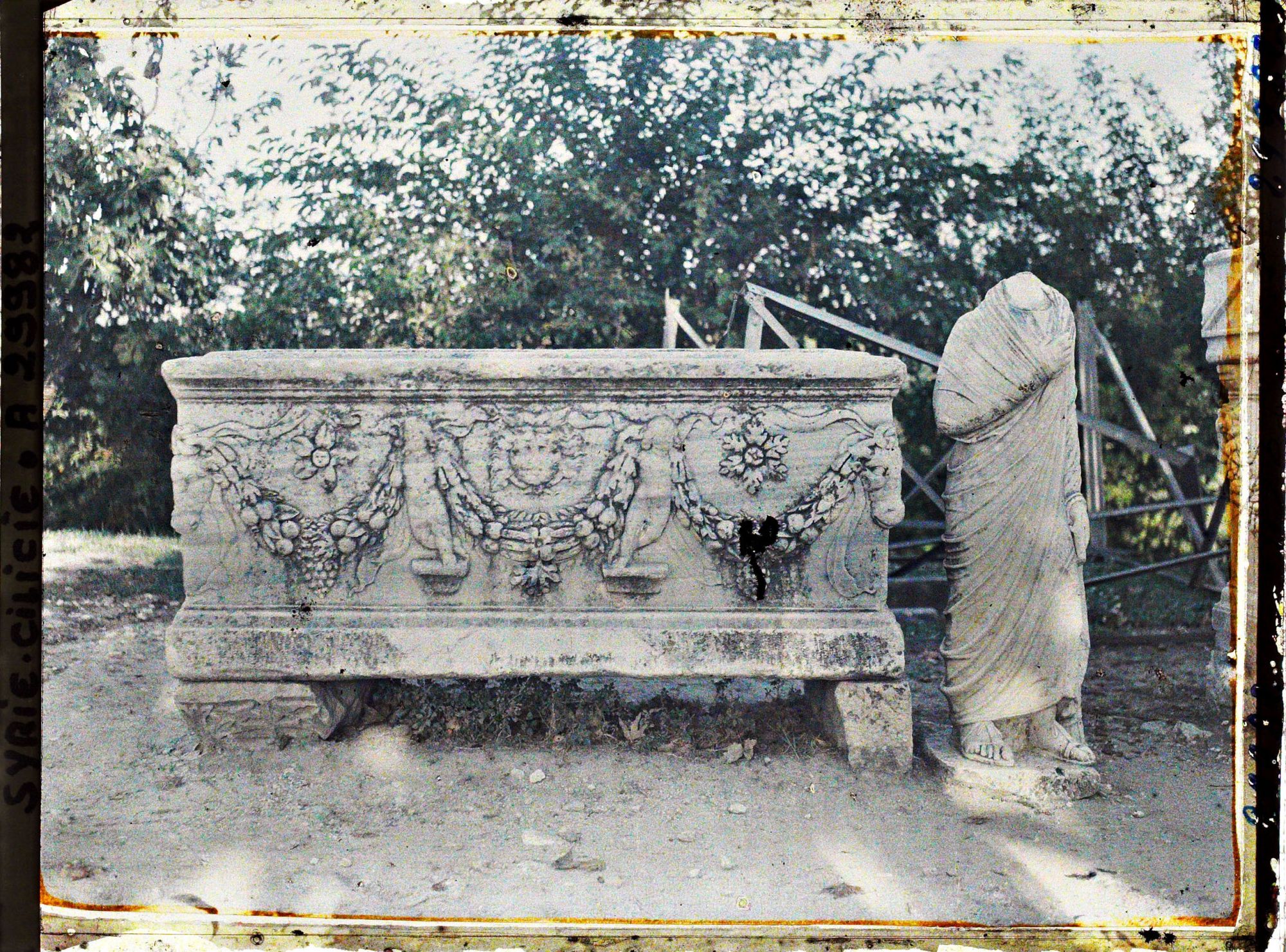 Image représentant Sarcophage romain représentant une décoration végétale, le soleil et Cupidon. A sa droite, une statue acéphale