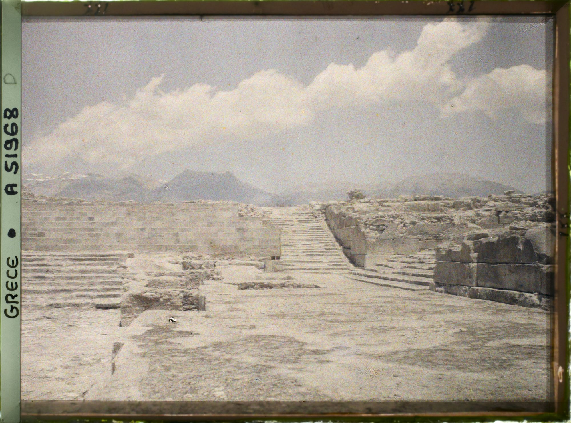Image représentant Le palais dans la cour occidentale, les gradins d'un théâtre. Au centre, l'escalier nord. A droite, le grand escalier (menant aux grands Propylées)