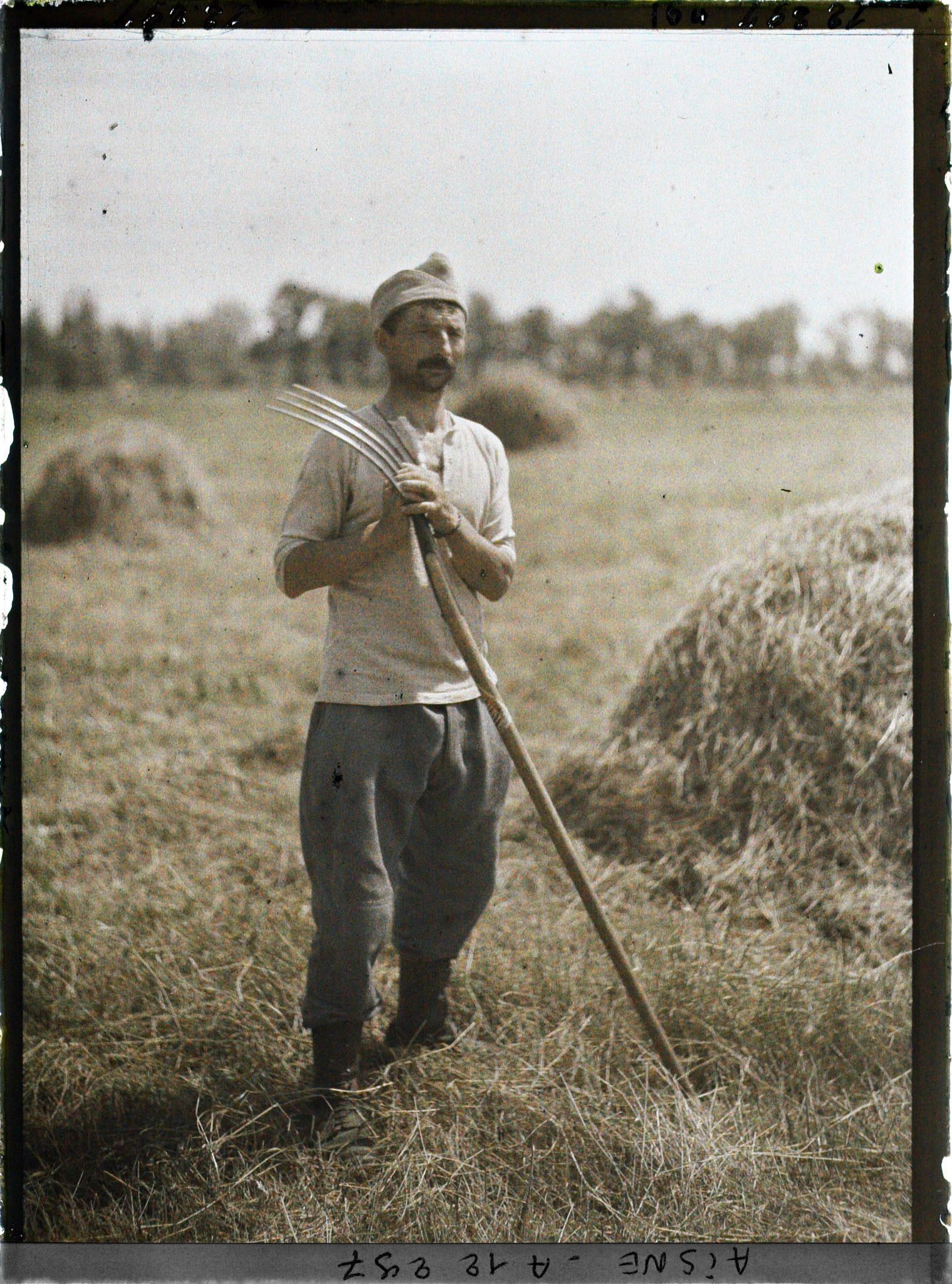 Image représentant Soldat posant avec une fourche devant des meules de foins