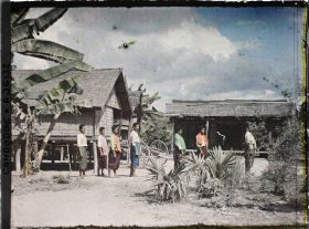 Image représentant Des villageois d'ethnie badak, en sampots larges, de profil devant quelques habitations