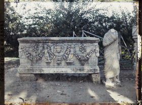 Image représentant Sarcophage romain représentant une décoration végétale, le soleil et Cupidon. A sa droite, une statue acéphale