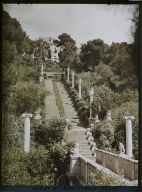 Image représentant La villa Cypris dominant le grand escalier fleuri du jardin ponctué de sculptures et la passerelle