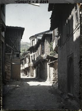 Image représentant Rue étroite pavée, bordée de maisons. Celles du fond à droite sont à encorbellement