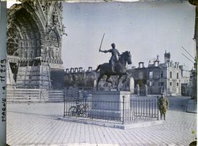 Image représentant Un poilu pose à côté de la statue de Jeanne d'Arc, (au fond la cathédrale et le palais du Tau), place du cardinal Luçon
