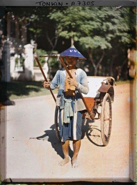 Image représentant Un pousse-pousse à roues caoutchoutées et son tireur, vêtu et coiffé de bleu