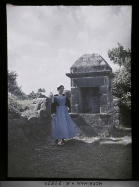 Image représentant Une Bretonne en costume traditionnel posant devant un puits, sur la route d'Auray à Carnac