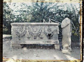 Image représentant Sarcophage romain représentant une décoration végétale, le soleil et Cupidon. A sa droite, une statue acéphale